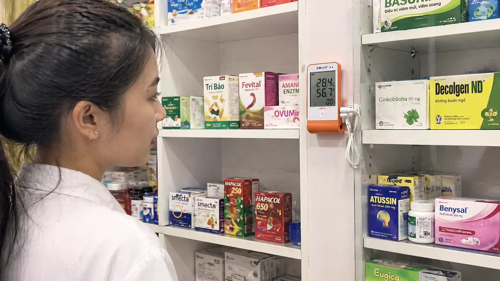 Dược sĩ đang kiểm tra nhiệt ẩm kế tự ghi lắp đặt trên kệ thuốc nhà thuốc chuẩn GPP
